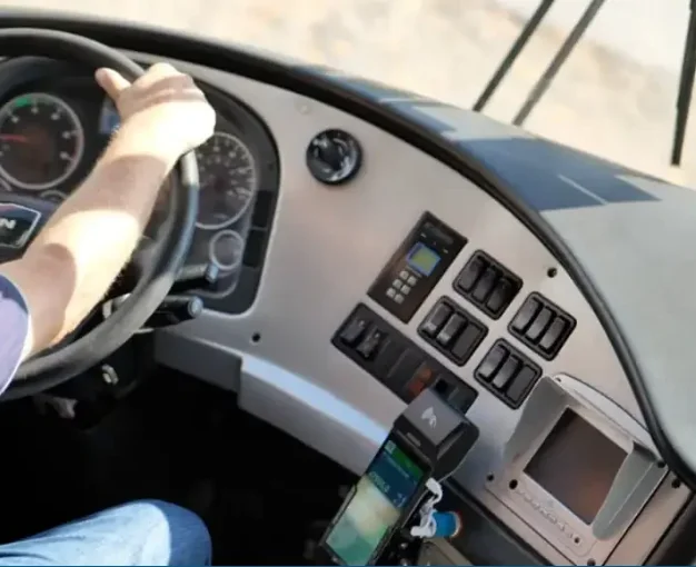 Padre de familia revisando en su celular la ubicaci&oacute;n segura de su camioneta van mediante app de rastreo GPS. Prompt IA: Fotograf&iacute;a realista de un padre de familia latino, vestido casual, mirando su smartphone con tranquilidad y una sonrisa leve. En el fondo, desenfocado pero reconocible, se ve su camioneta van o pickup estacionada segura fuera de una casa bonita. Iluminaci&oacute;n de d&iacute;a, c&aacute;lida. Transmite paz mental y control.
